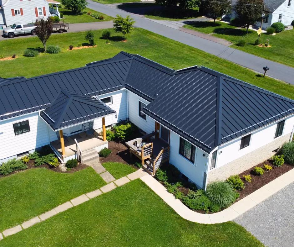 Aerial view of a modern home with a black metal roof, landscaped yard, and stone pathway, showcasing a welcoming entrance and community-oriented design.